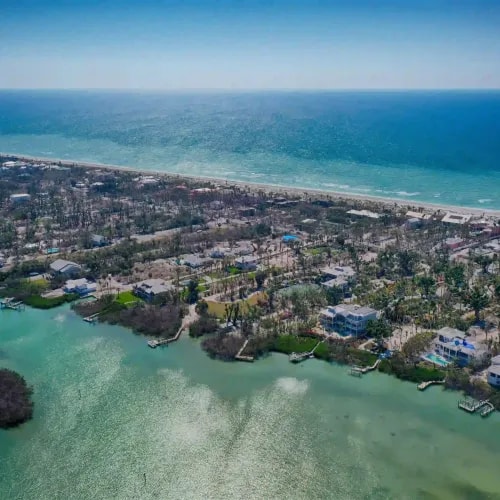 Aerial view of beachfront development with waterfront homes and dense vegetation along a coastal edge