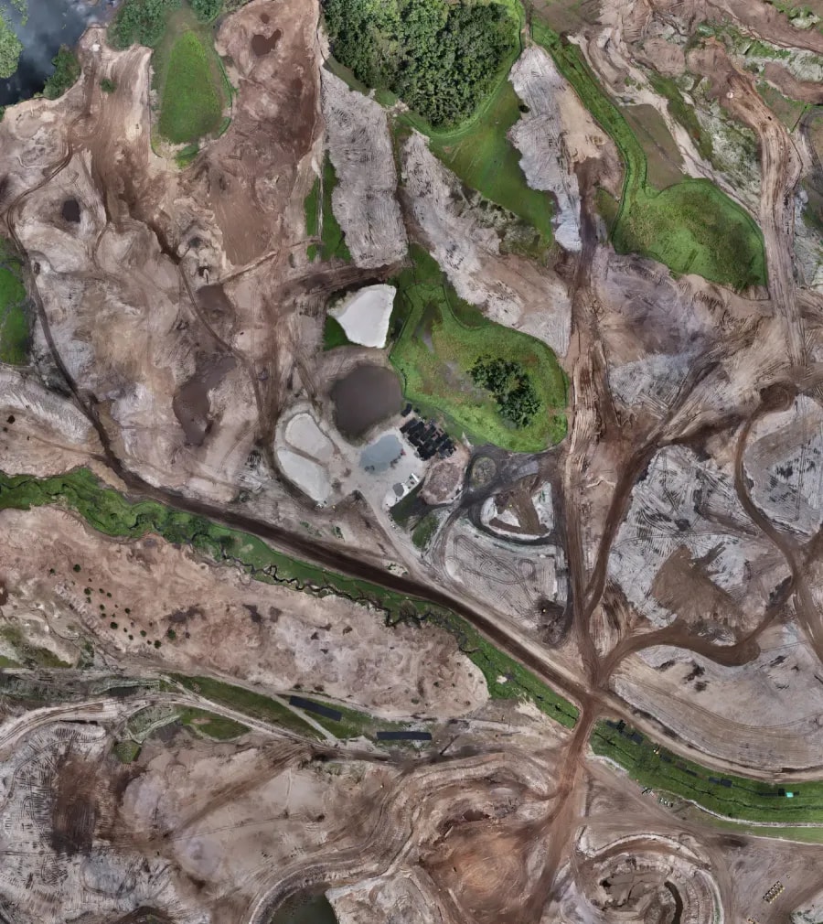 High-resolution aerial view showing complex terrain patterns, sand features, vegetation patches, and water drainage across a golf course site under development