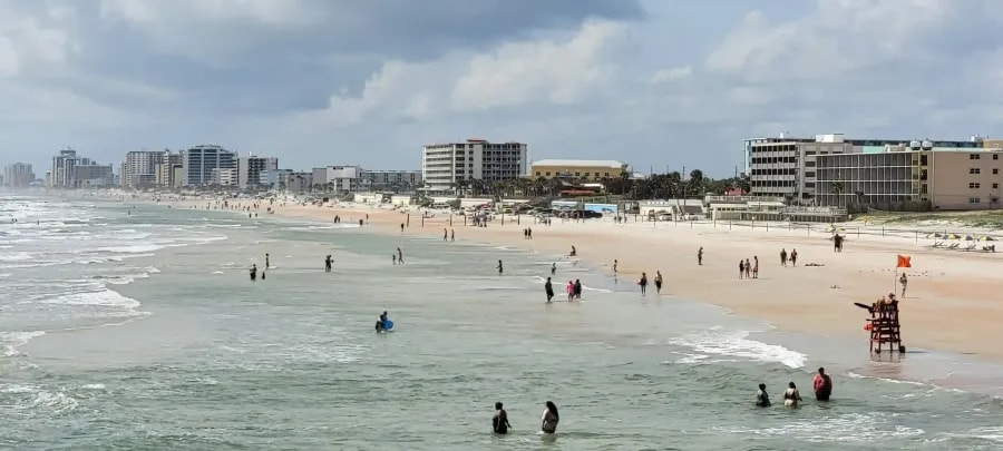Wide view of a populated urban beach with ocean waves, people swimming, and high-rise buildings along the shore