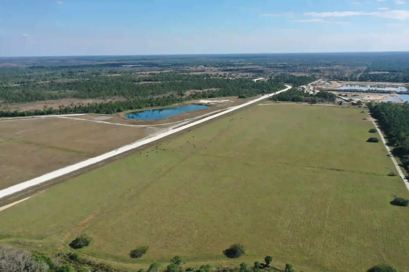 Aerial view of flat rural terrain with dirt roads, natural ponds, and scattered vegetation in the background