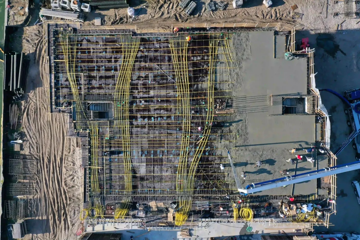 Top-down aerial view of an active construction site with rebar grids and workers pouring concret