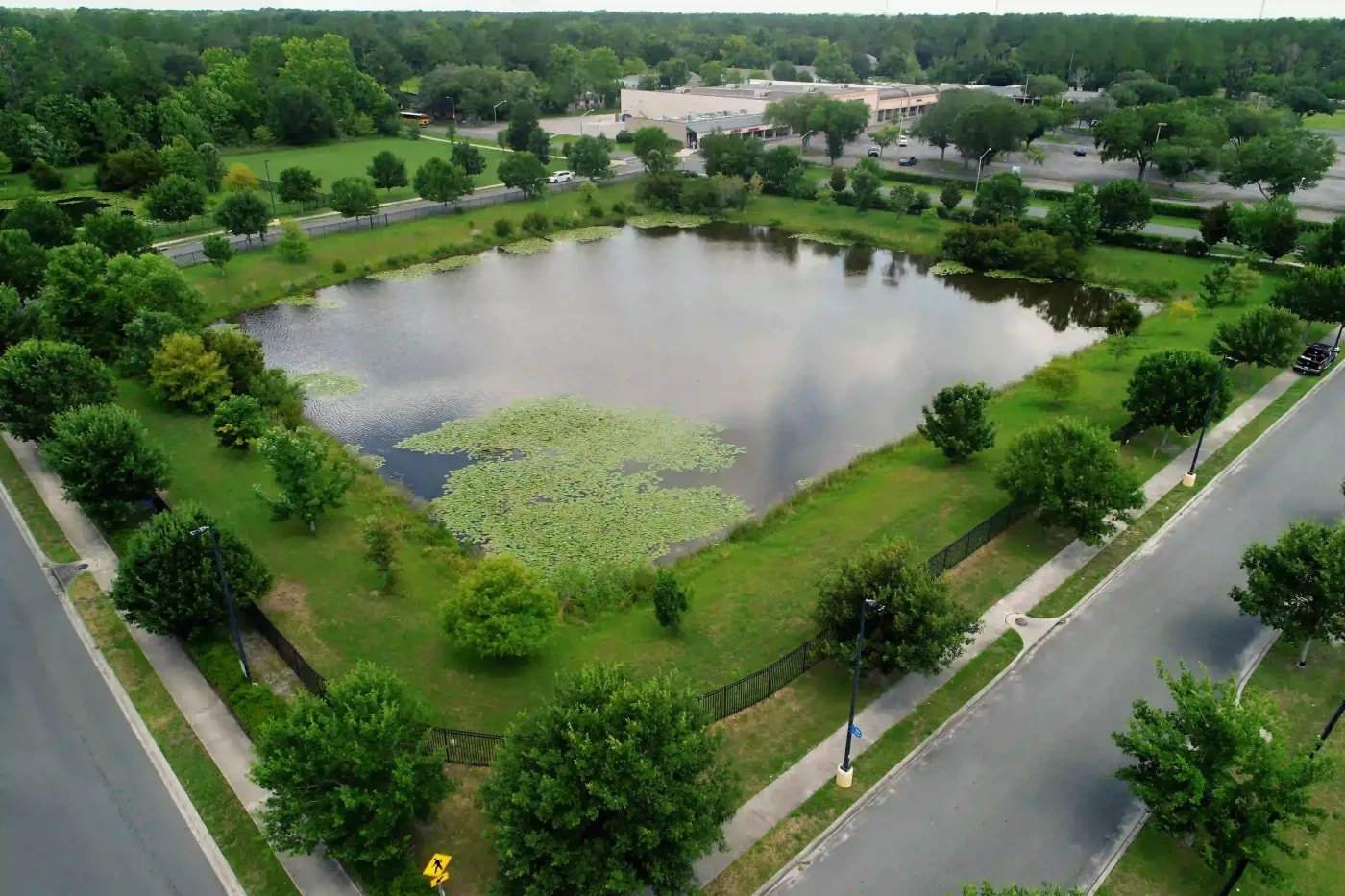 Drone photo of a stormwater retention pond bordered by trees, walkways, and nearby retail spaces