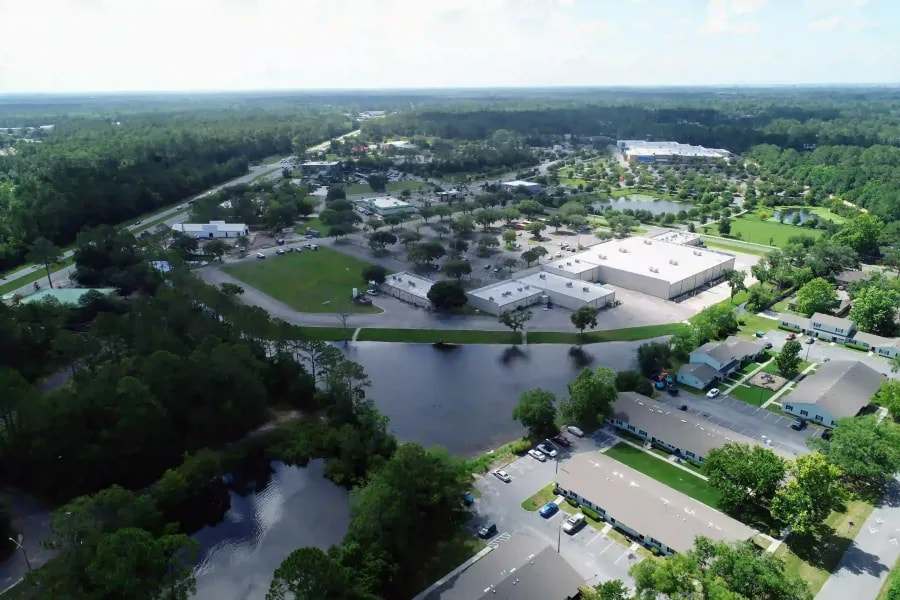 Aerial view of a suburban shopping center surrounded by wooded areas, small lakes, and residential buildings