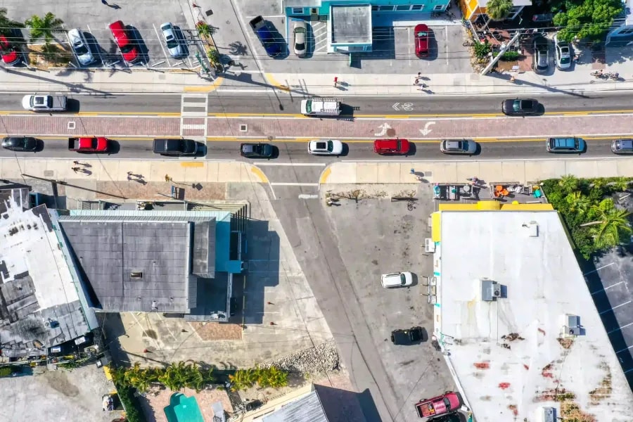 op-down drone view of a commercial street with vehicles, crosswalks, and mixed-use buildings in a coastal town setting