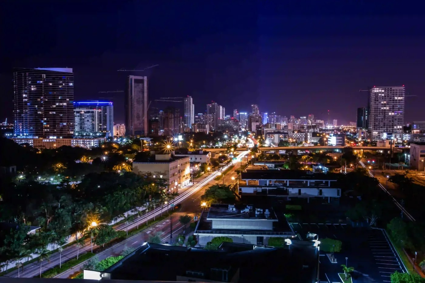Nighttime cityscape featuring high-rise buildings, light trails, and dense urban infrastructure under construction