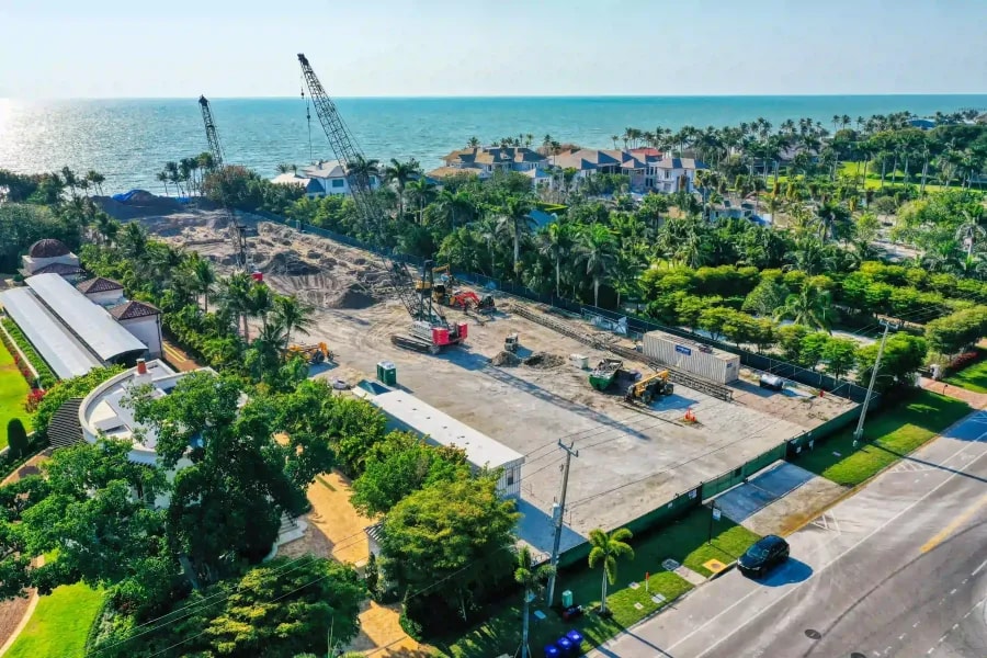 Seaside construction site with excavation equipment, palm-lined streets, and upscale homes in a coastal development