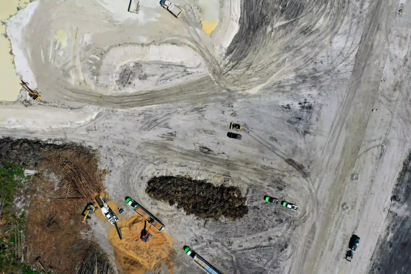 Top-down drone image of a sandy industrial site with heavy machinery and dump trucks working on land clearing