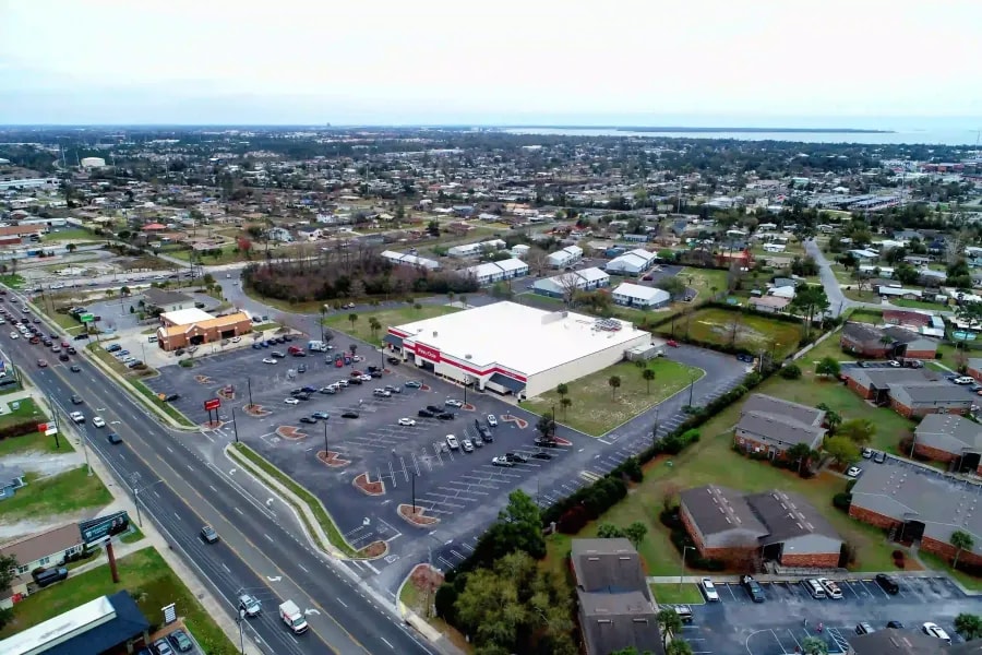 Aerial view of a retail shopping center surrounded by suburban homes and a major highway in Panama City Beach