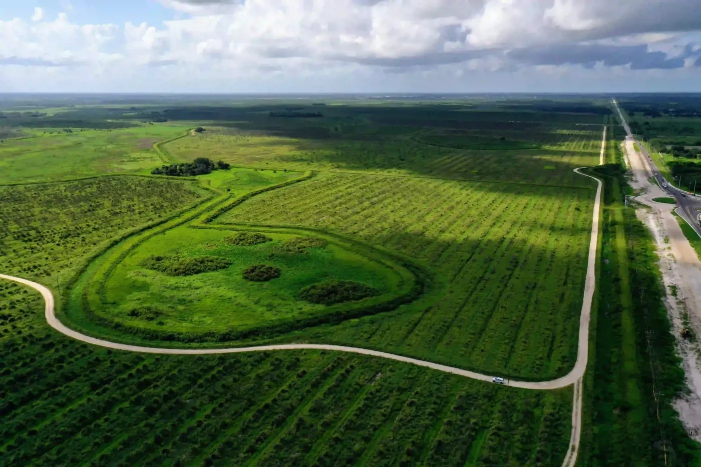 Aerial landscape of farmland with neat crop rows, curving access roads, and patches of green under dramatic sky