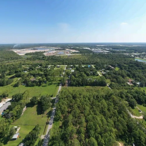 Drone photo of a semi-rural area with scattered homes, open land, and industrial development visible on the horizon