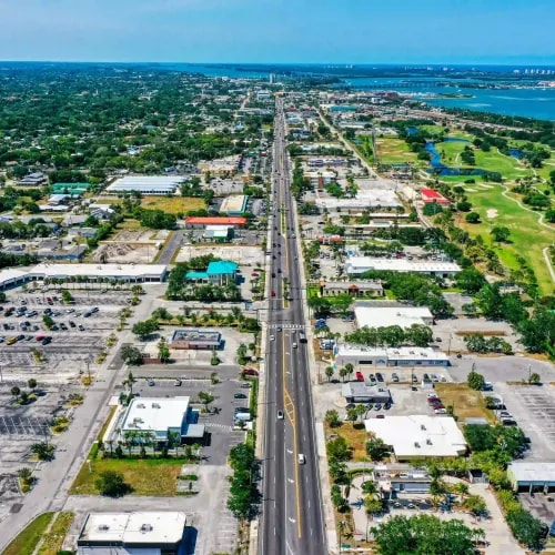 Aerial photo of a commercial boulevard flanked by retail centers, a golf course, and a coastal bridge in the distance