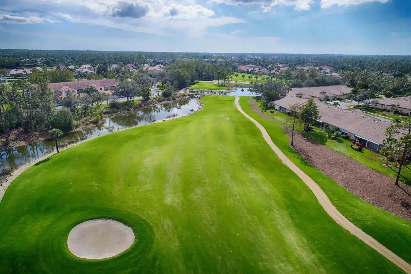 Aerial shot of a golf course with a sand bunker, adjacent water channel, and nearby residential lots