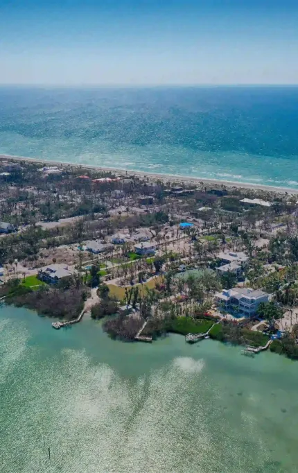 Aerial view of beachfront development with waterfront homes and dense vegetation along a coastal edge