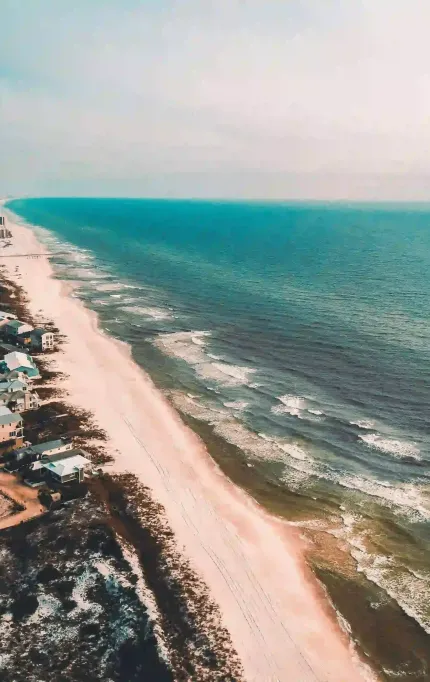 Drone shot of coastal homes along white-sand beach with turquoise waters and residential development