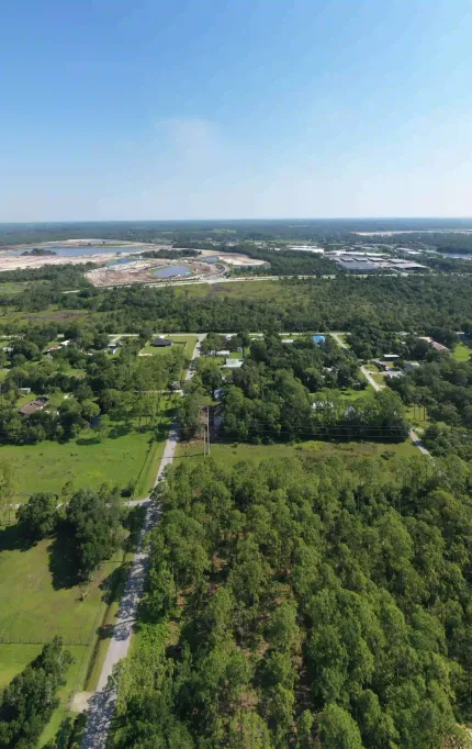 Drone photo of a semi-rural area with scattered homes, open land, and industrial development visible on the horizon