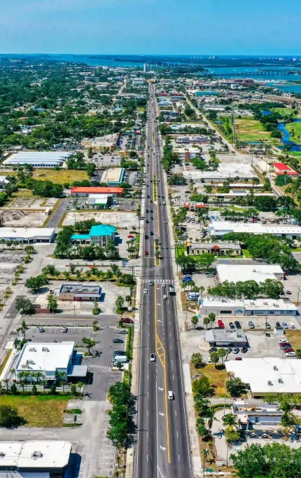 Aerial photo of a commercial boulevard flanked by retail centers, a golf course, and a coastal bridge in the distance
